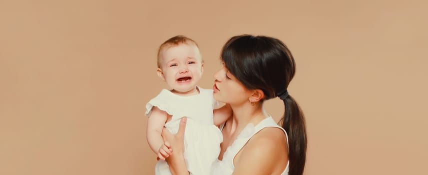 young mother holding sad crying baby on brown studio background