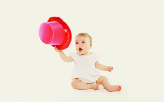 Happy cheerful baby playing with pink hat on the floor on white studio background