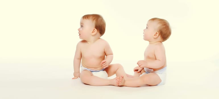 Cute two twin babies in diapers sitting on the floor on white studio background