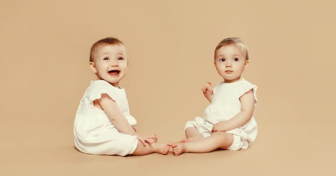 Portrait of happy cute two twin babies sitting on the floor on brown studio background