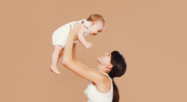 Happy cheerful smiling young mother playing with cute baby on brown studio background