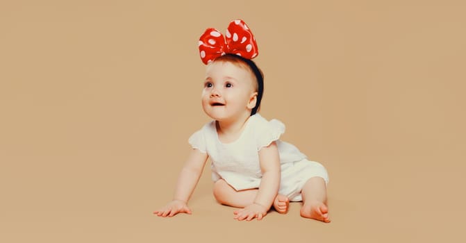 happy cute baby with bow on the head crawling on the floor on brown studio background