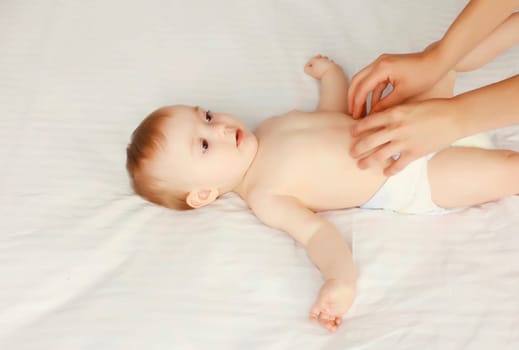 mother gives massage to baby lying on the bed at home, child and health concept