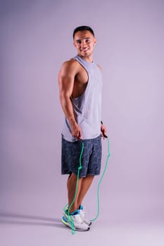 Young man exercising with skipping rope and looking at the camera isolated on grey background
