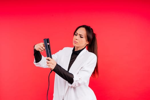 Happy young woman with beautiful hair holding curling iron on a grey and red background