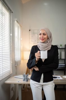 Business woman muslim. confident businesswoman muslim in hijab standing with morning coffee mug in office.