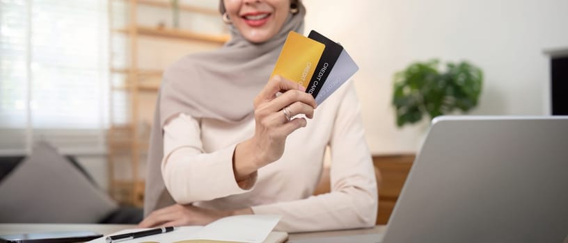 Young woman using laptop at home shopping online. Muslim woman wearing hijab using laptop and holding credit card. Internet banking concept. Muslim woman online shopping.