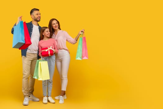 A cheerful family presenting a gift and holding shopping bags, showcasing a consumer lifestyle on a yellow backdrop