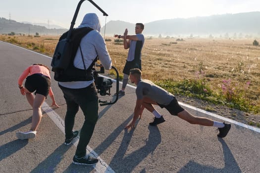 A skilled videographer captures the dynamic scene as athletes engage in warming up and stretching exercises in preparation for their morning run, showcasing dedication and teamwork behind the lens.