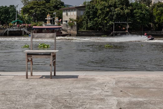 The old wooden chair is in front of the river, which is on the cement floor. Copy space, Selective focus.