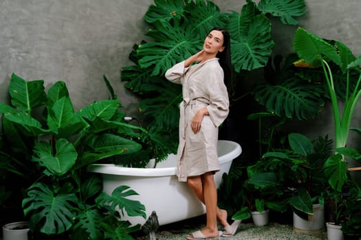 Tropical and exotic spa garden with bathtub in modern hotel or resort with young woman in bathrobe enjoying leisure and wellness lifestyle surrounded by lush greenery foliage background. Blithe