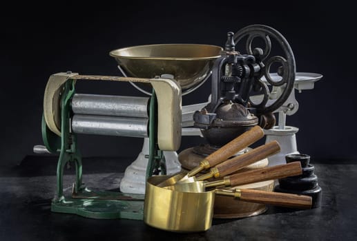 Antique collection has Pasta maker with hand crank, Original coffee grinder metal shake wheel with hand crank, Weight scale and Brass Measuring Cups on Dark background. Copy space. Selective focus.