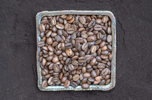 Coffee beans in ceramic square bowl with Coffee powder background. lternative coffee for living life, Coffee concept, Space for text, Selective focus.