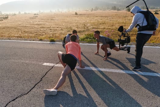 A skilled videographer captures the dynamic scene as athletes engage in warming up and stretching exercises in preparation for their morning run, showcasing dedication and teamwork behind the lens.