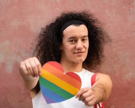 Portrait of happy gay man holding a rainbow heart shape to support LGBTQ community isolated on vintage background.