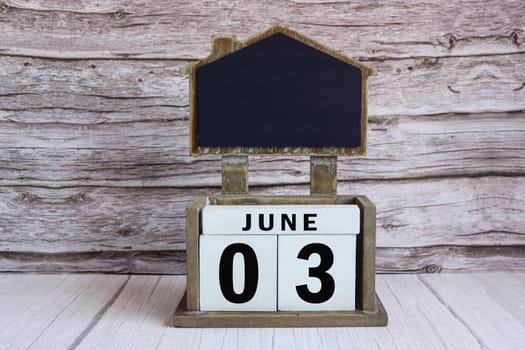 Chalkboard with June 03 calendar date on white cube block on wooden table.