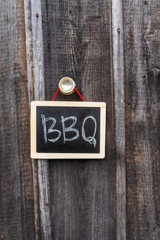 A rustic chalkboard with BBQ written hangs on a wooden wall
