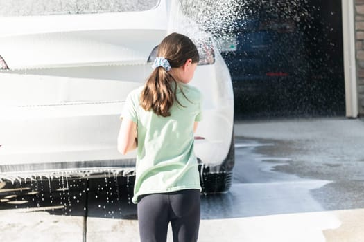 A young girl enthusiastically assists in washing the family's electric car in their suburban driveway.