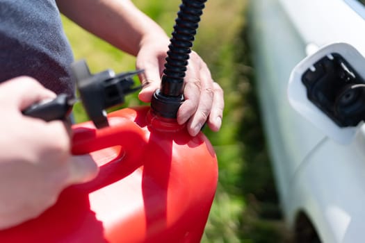 A person refills a car s tank with a red gas can on a sunny day