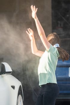 A young girl enthusiastically assists in washing the family's electric car in their suburban driveway.