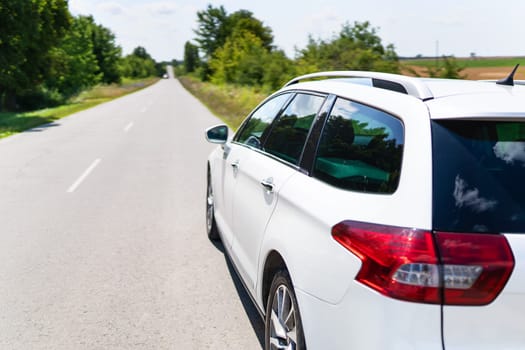 A white car is parked on a sunny road, ready for a journey amidst greenery and clear skies. The scene exudes tranquility and adventure