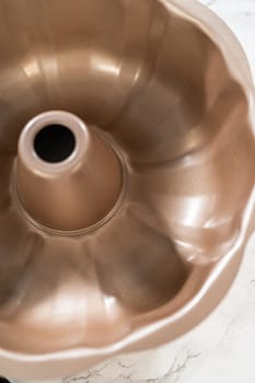 Using a silicone brush, the metal bundt cake pan is greased with melted vegetable shortening, preparing for baking the scrumptious Carrot Bundt Cake.