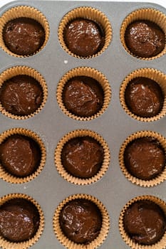 The process involves carefully scooping the rich batter into the waiting cupcake pan.