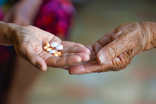 A caregiver's hand gently transferring assorted pills to an elderly person's open palm, symbolizing care and support