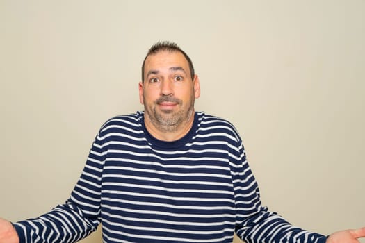 Hispanic man with beard in his 40s isolated on beige background doubting and shrugging shoulders in questioning gesture.
