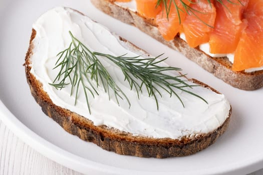 Rye sandwich with cream cheese and salmon on white wooden table.