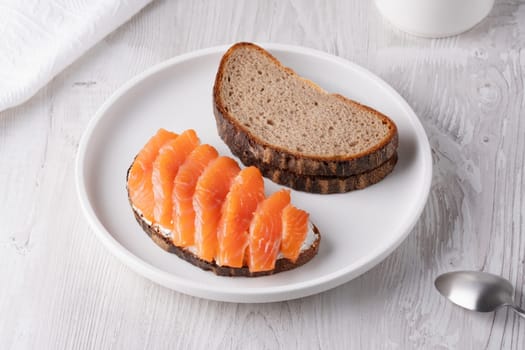 Rye sandwich with salmon and cream cheese on white wooden table.