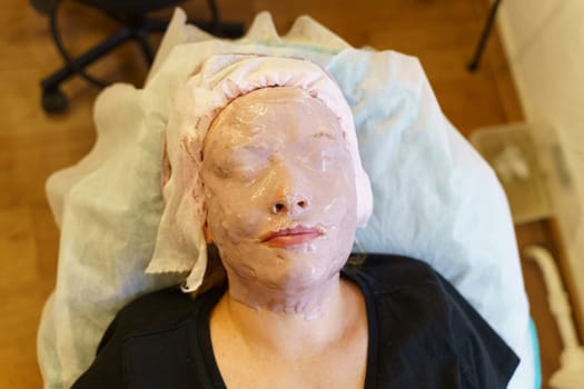 A woman having a facial mask applied during a skincare treatment at a beauty salon.