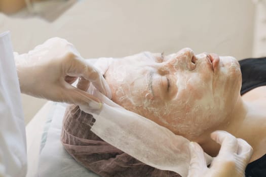 A woman having a facial mask applied to her face by a professional at a spa. The mask is being carefully smoothed onto her skin for a skincare treatment.