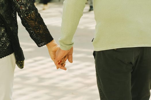 Two individuals walking hand in hand, strolling down a city street with buildings in the background.