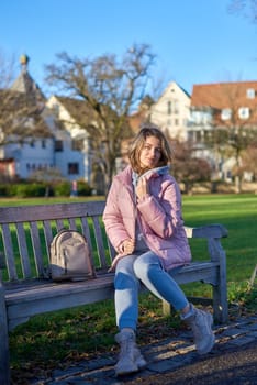 Embrace the tranquility of winter with this captivating image featuring a beautiful girl in a pink winter jacket, leisurely sitting on a bench in a park against the backdrop of a charming old European town. The photograph beautifully captures the serene atmosphere, blending the girl's winter style with the timeless charm of the historic surroundings. Winter Wonderland Elegance: Beautiful Girl in Pink Jacket Enjoys Festive Atmosphere in Bitigheim-Bissingen Park. Experience the magic of the holiday season as a charming girl in a pink winter jacket sits on a bench in a park against the backdrop of the historic town of Bitigheim-Bissingen, Baden-Württemberg, Germany. The scene is adorned with picturesque half-timbered houses, creating a delightful blend of winter charm and architectural beauty.