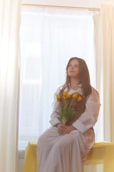 Beautiful sweet girl in nightgown in early morning with bouquet of delicate yellow tulips. Gift on International Women's Day on March 8th. Cosmetics, skin and hair care. Perfume, natural fragrance