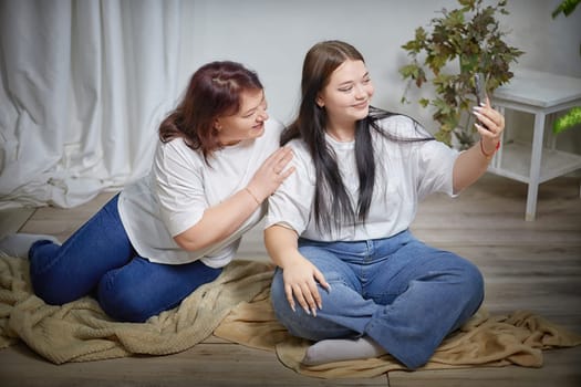 Fat funny funny adult mother and daughter posing, taking selfies indoors. Body positive, friendly family in the room