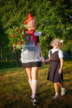 Young and adult schoolgirl on September 1 with flowers. Generations of schoolchildren of USSR and Russia. Female pioneer in red tie and October girl in modern uniform. Daughter and Mother having fun