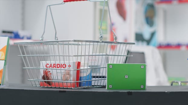 Basket filled with medicaments and a box with greenscreen layout at pharmacy cash register counter. Empty drugstore having pharmaceutics and package with isolated copyspace mockup.