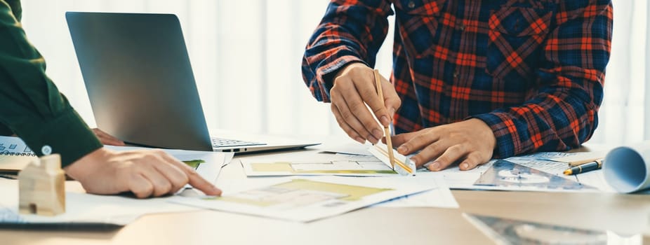 A portrait of skilled architect engineer hand writing a detail of blueprint during male engineer searching data from laptop at modern architectural office. Focus on hand. Closeup. Delineation.