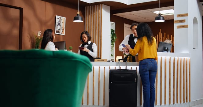 Front desk staff assisting women with registration process, asking to see passport and sign confirmation documents for accommodation. Two guests arriving at five star holiday retreat.