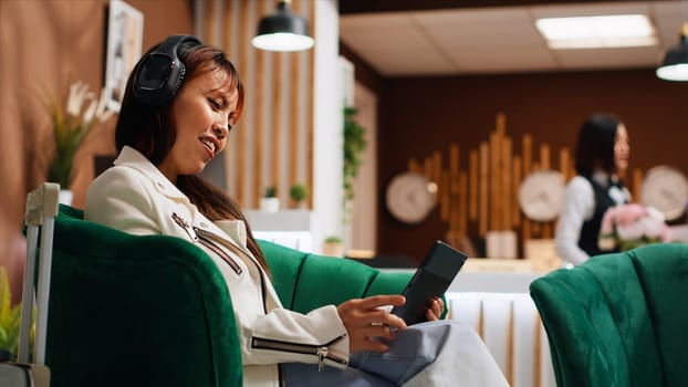 Traveler using tablet to pass time in lounge area at hotel, watching movies or searching for places to visit during stay. Asian woman browsing on internet pages, tourism concept. Handheld shot.