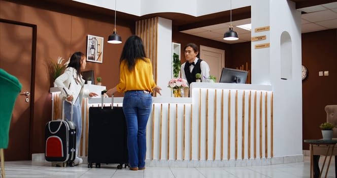 Asian tourists entering hotel lobby and using service bell, ringing to call employees and offer support at check in. Travelers requesting assistance from front desk staff, hospitality industry.