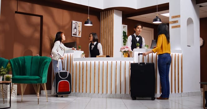 Asian guests approach reception to ask about accommodation, arriving at hotel and hoping for an early check in. Front desk staff team welcoming women and offering their services. Tripod shot.