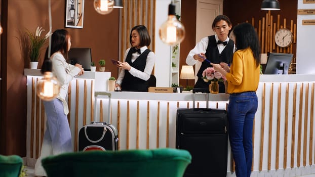 Women going through registration process at front desk, hotel staff team checking passport information for registration. Travelers signing reservation forms for accommodation. Handheld shot.