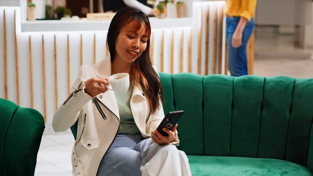 Modern person taking advantage of free wifi in lobby, using smartphone to pass time before going through check in process. Asian woman scrolling on social media apps, tourism concept.