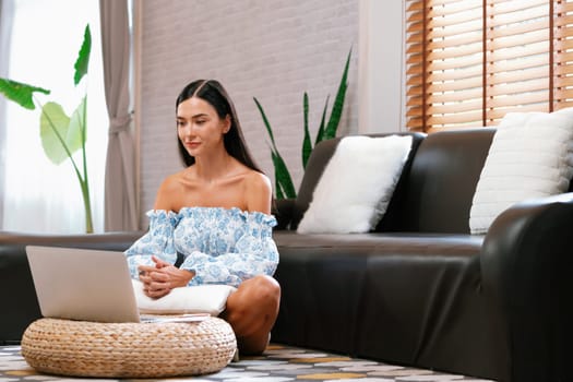 Young woman using laptop, happily browsing the internet or making online purchases on sofa at home. Modern woman enjoying her domicile lifestyle by studying online or simply relaxing. Blithe