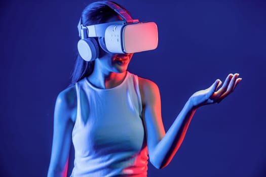 Smart Female standing surrounded by neon light wear VR headset connecting metaverse, futuristic cyberspace community technology. Elegant woman use hand holding generated virtual object. Hallucination.