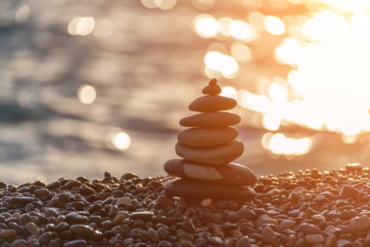 Balanced rock pyramid on pebbles beach. Golden sea bokeh on background. Selective focus, zen stones on sea beach, meditation, spa, harmony, calm, balance concept