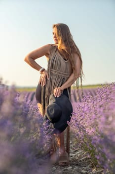 A woman is standing in a field of purple flowers, wearing a black dress and a black hat